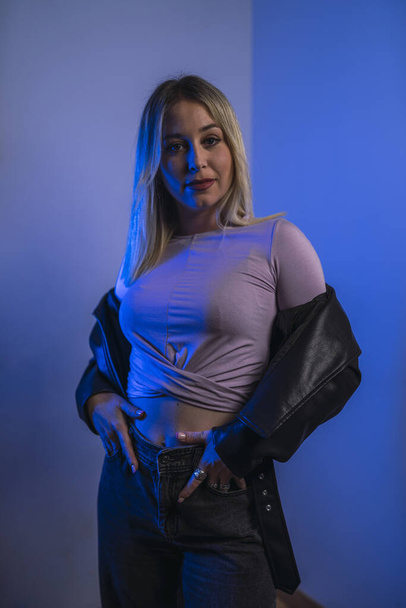 An attractive Caucasian female from Spain in a leather jacket posing in a studio with blue lights - Fotoğraf, Görsel