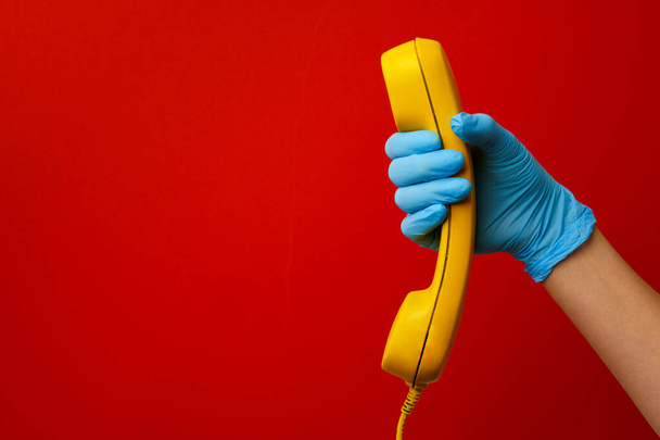Female hand in medical glove holding yellow telephone speaker - 写真・画像