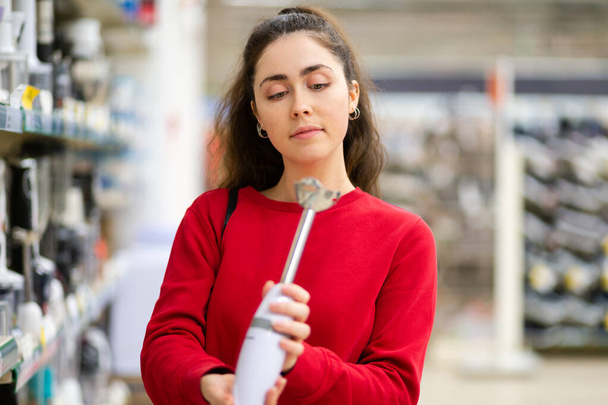 A young woman chooses a blender in a home appliance store. Side view. The concept of consumerism and shopping. - Photo, image