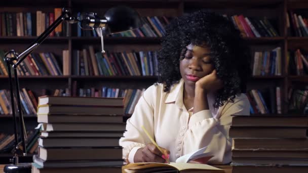 Afro-Amerikalı kadın yarı karanlık odadaki masada yazıyor. - Video, Çekim