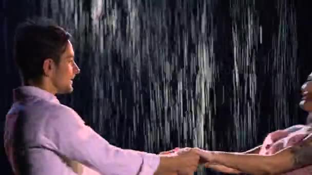 Happy loving couple whirls holding hands on the background of the rain. The love story of a man and a woman. A romantic date in the rain in the dark. Close up. - Imágenes, Vídeo