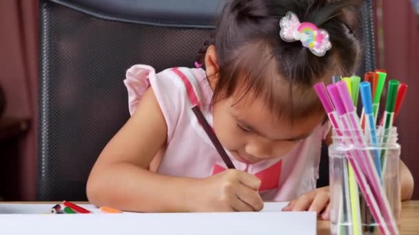 Een schattig klein meisje tekent een regenboog op papier met gekleurde potloden aan de tafel thuis. - Video