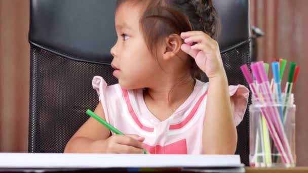 Söpö pikkutyttö piirtää sateenkaaren paperille värillisillä kynillä kotona pöydässä.. - Materiaali, video