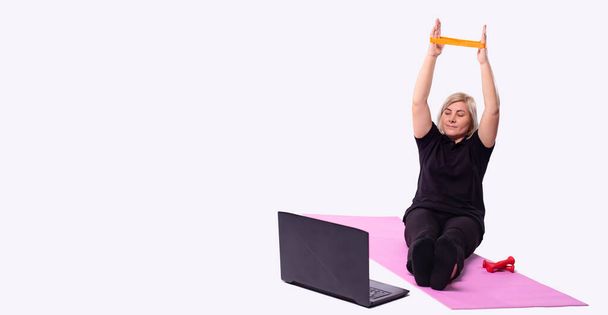 Banner, long format.Handsome elderly woman watching online workout on laptop and using elastic rope band during morning training, grey background. High quality photo - Fotografie, Obrázek
