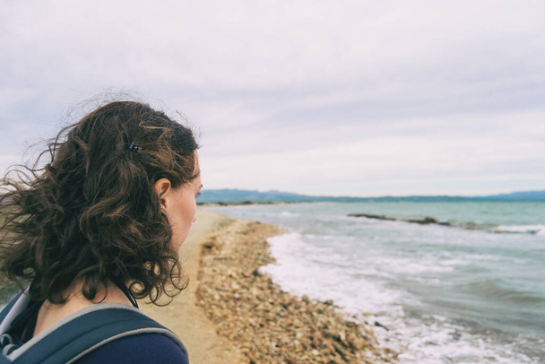 κορίτσι που κοιτάζει τη θάλασσα σε μια συννεφιασμένη και θλιβερή μέρα με την άγρια θάλασσα - Φωτογραφία, εικόνα