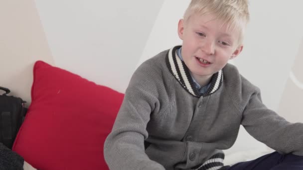 hermoso niño melancólico rubio en un suéter se sienta en casa en el sofá - Imágenes, Vídeo