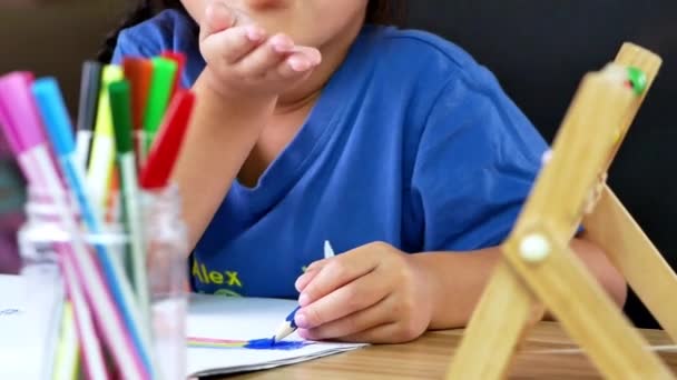 Słodka dziewczynka rysuje tęczę na papierze z kolorowych ołówków przy stole w domu. - Materiał filmowy, wideo