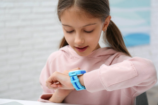 Girl with stylish smart watch at table indoors - Foto, Bild