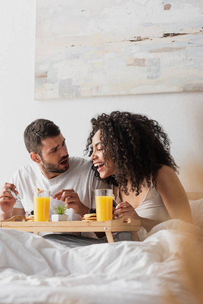 shocked bearded man looking at happy african american girlfriend having breakfast  - Fotó, kép
