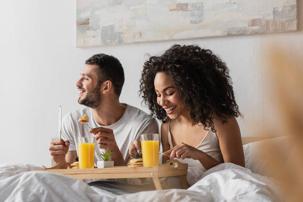 cheerful multiethnic couple eating breakfast in bed  - Фото, зображення