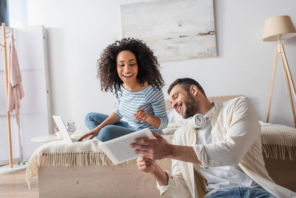 multiethnic couple looking at digital tablet in bedroom  - Foto, afbeelding