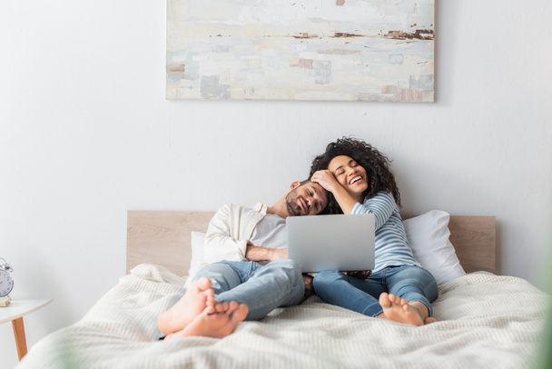 interracial couple smiling and chilling on bed while watching movie on laptop - Foto, Imagen