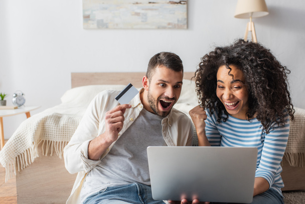 amazed interracial couple looking at laptop while shopping online  - Photo, Image