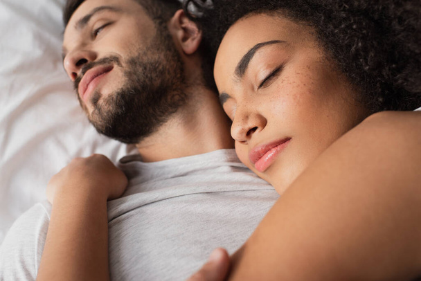 close up of curly african american woman hugging bearded man and lying in bedroom  - Φωτογραφία, εικόνα