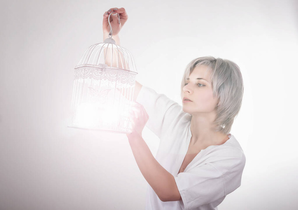 νεαρή ξανθιά γυναίκα παίρνει ένα φως σε ένα κλουβί πουλιών - Φωτογραφία, εικόνα