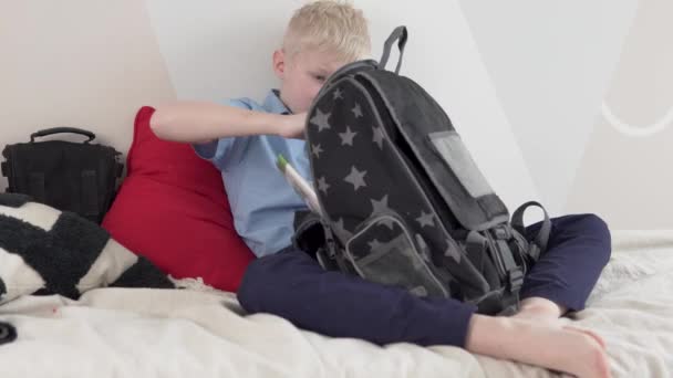 Un garçon écolier vérifie les manuels scolaires dans un sac à dos scolaire à la maison devant l'école - Séquence, vidéo