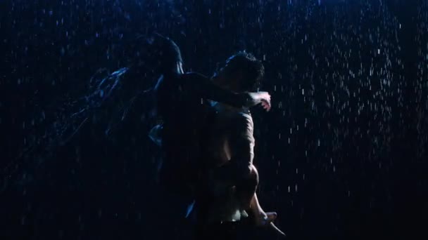 Happy lovers perform dance of passion in rain and enjoy each other. Water runs down wet clothes and bodies and sparkles in studio light. Love story of happy couple. Silhouettes. Close up. Slow motion. - Video