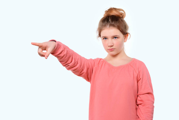 Proszę spojrzeć. Zaskoczona młoda dziewczyna w różowej, luźnej bluzie wskazującej palcem na bok. Stojąc nad białym tle studio - Zdjęcie, obraz
