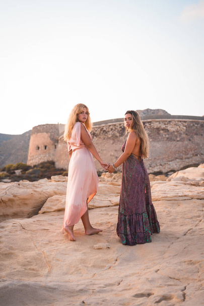 A couple of Caucasian girls with pink dresses, on the beach by the sea, walking along the Playazo de Rodalquilar in Cabo de Gata - Foto, Imagen