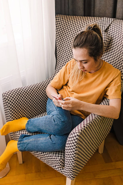Young woman with smartphone sitting in the comfortable armchair at hom - Foto, Imagen
