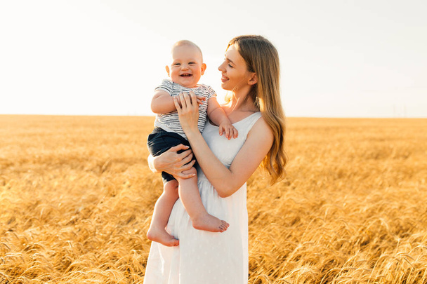 Schöne junge Mutter mit Baby im Weizenfeld, Glückliche Familie im Sonnenuntergang, Muttertag - Foto, Bild