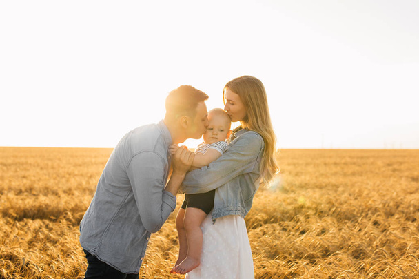 Happy family, mother, father and little child on the ripe wheat field at sunset - Foto, imagen