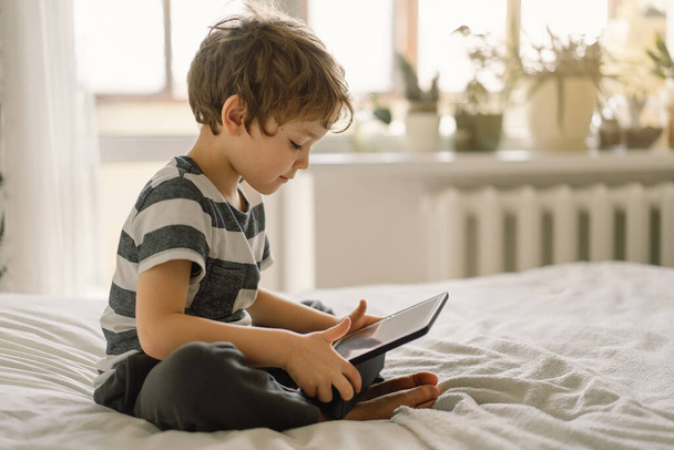 Kisfiú egy tablettel a szobában. A fiú játszadozik a tableten. Technológiai koncepció. Gyermek egy modullal - Fotó, kép