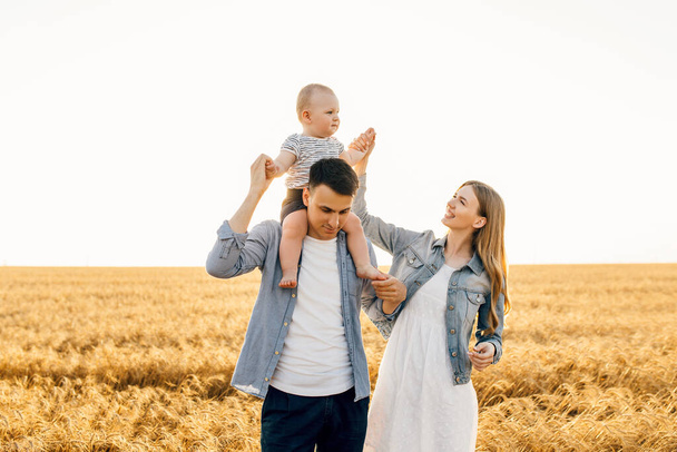 Happy family, mother, father and little child on the ripe wheat field at sunset - Fotografie, Obrázek