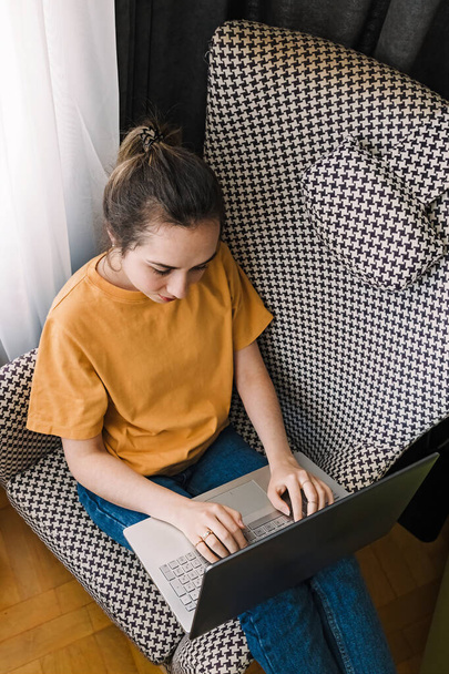 jonge vrouw zitten in gezellige stoel met haar laptop - Foto, afbeelding