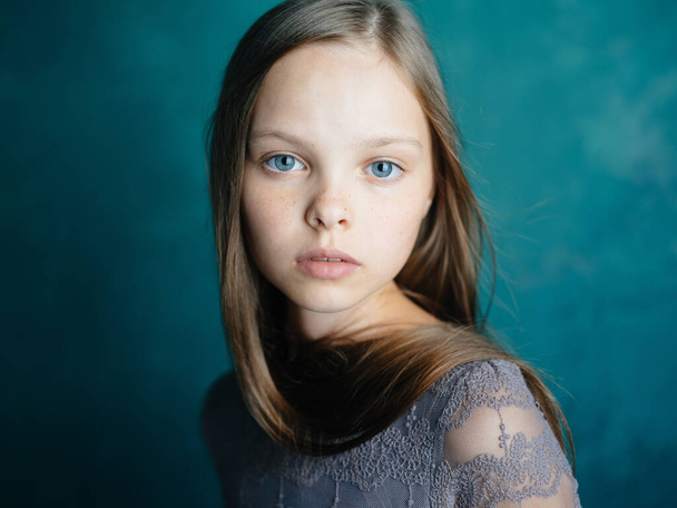 Portrait of a beautiful little girl in a gray dress on a blue background close-up cropped view of the model - 写真・画像