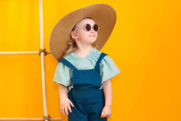Happy little girl, the child is enjoying the summer. Soon on vacation and she is packing for a trip. He tries on sun glasses , a hat, and drinks juice. - Photo, Image