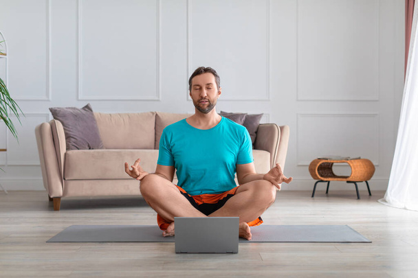 Мужчина медитирует перед монитором ноутбука. - Фото, изображение