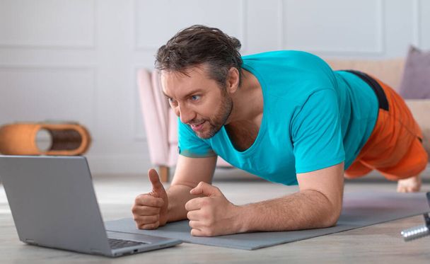 Fotografía de cerca de un hombre de mediana edad haciendo el ejercicio de tablón. Sigue la guía en línea a través de smartphone. - Foto, Imagen