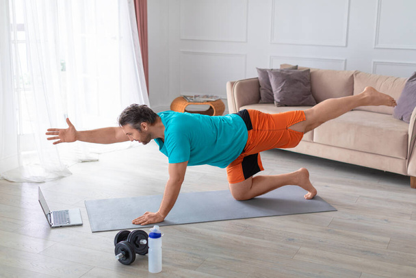 Online edzések otthon. Fénykép egy középkorú férfi során egyensúly képzés előtt egy laptop monitor. - Fotó, kép