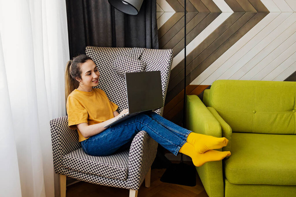 Young woman sitting in cozy chair with her laptop - Foto, afbeelding