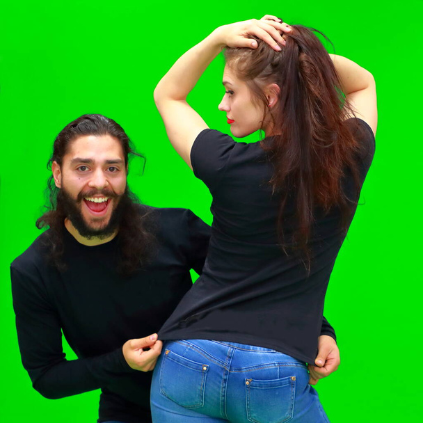 Attraktive Frau und junger Mann stehen fröhlich lächelnd auf dem grünen Chroma-Schlüsselhintergrund. Auf dem T-Shirt des Mädchens ist ein weißer Fleck für Werbeinhalte. - Foto, Bild