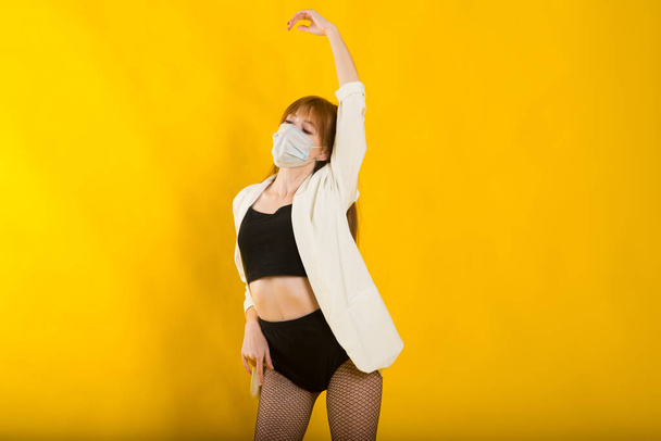 Samičí striptérka ve žlutém ateliéru v ochranné masce z kovidu, černý bodysuit - Fotografie, Obrázek