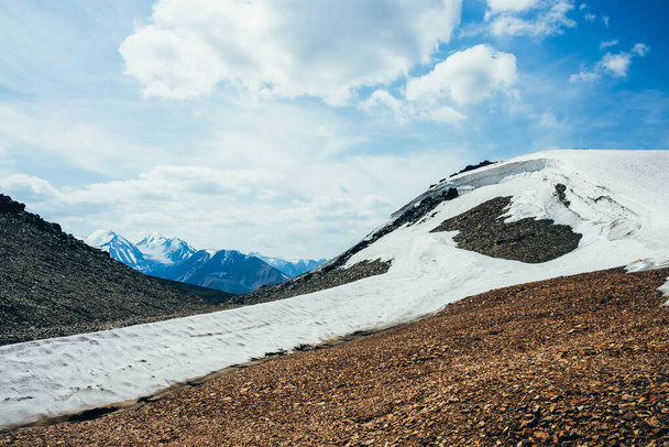 Prachtige kleine gletsjer met ijskap op steenachtige heuvel onder bewolkte hemel. Sneeuw op de berg. Vuur op steen. Sfeervol alpenlandschap op grote hoogte. Prachtig hoogland landschap van majestueuze natuur. - Foto, afbeelding