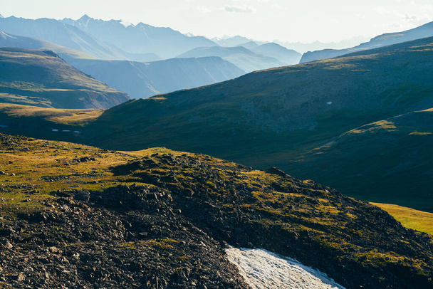 Levendig landschap met kleine gletsjer op de helling op de achtergrond van gigantische rotspartijen en diepe kloof achter groene vallei en heuvel in het zonlicht. Sneeuw op de helling en grote rotsen. Geweldig zonnig uitzicht op de grote bergen. - Foto, afbeelding