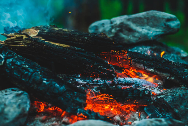 Vivid smoldered firewoods burned in fire close-up. Atmospheric warm background with orange flame of campfire and blue smoke. Unimaginable full frame image of bonfire. Burning logs in beautiful fire. - Photo, Image