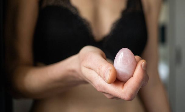 woman holding in hand a vaginal (yoni) egg. Rose quartz crystal jade egg.  - 写真・画像