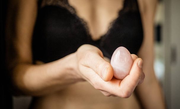 woman holding in hand a vaginal (yoni) egg. Rose quartz crystal jade egg.  - Zdjęcie, obraz