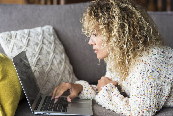 Giovane donna adulta a casa sdraiata sul divano e utilizzare il computer portatile per lavorare o navigare sul web  - Foto, immagini