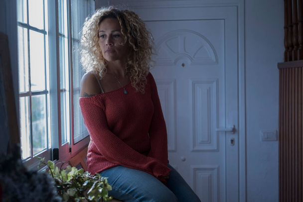 Θλιβερή γυναίκα μόνη στο σπίτι κοιτάζοντας έξω από το παράθυρο - πορτρέτο ενηλίκων γυναικών με θλίψη και μοναξιά κάθισε και περίμενε κοντά στην πόρτα - Φωτογραφία, εικόνα