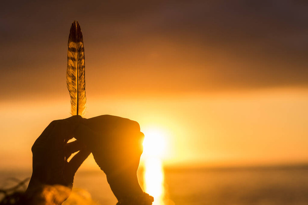 Traumleben und Hoffnung Zukunftskonzept mit Nahaufnahme der Hände hält eine Feder mit Sonnenuntergang Sonnenlicht im Hintergrund dabei Silhouette - Foto, Bild