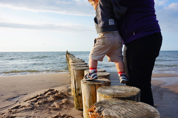 SIANOZETY, POLAND - Jul 21, 2015: Woman holding child on a row of wooden poles at the beach - Photo, Image