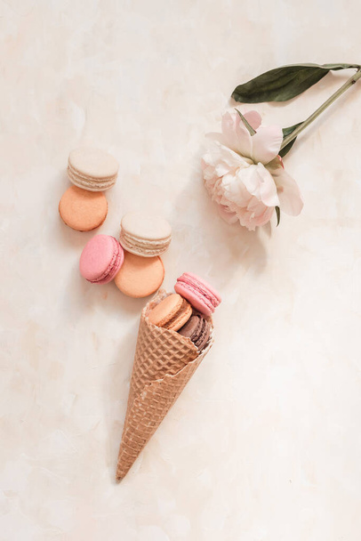 A top view of the sweet colorful macarons in the waffle cone on the light brown surface - Foto, Imagen