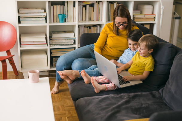 mother and kids using laptop computer while sitting on sofa at home - Fotografie, Obrázek