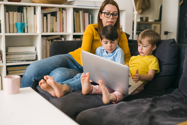 mother and kids using laptop computer while sitting on sofa at home - Φωτογραφία, εικόνα