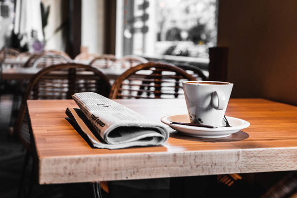 A closeup shot of a cup of coffee and a newspaper on the table in a cafe - Фото, зображення
